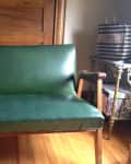 Green vinyl loveseat with wooden arms in a room with wooden floors, books, and a striped shopping bag.
