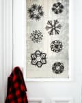 Black paper snowflakes on a frosted glass door with a red and black plaid shirt hanging on the side.