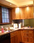 Wooden kitchen with granite countertops, stainless steel appliances, and a view into a sunlit dining nook with large windows.
