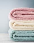 Stack of folded towels in pink, cream, and teal on a wooden surface.
