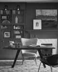 Home office with a wooden desk, bookshelves, armchair, and abstract art above a fireplace.