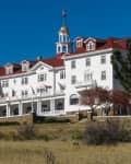 Historic white hotel with red roof, American flags, and a cupola, set against a clear blue sky and surrounded by trees.