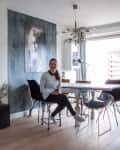 Modern dining room with a woman sitting at a table, black chairs, ornate mirror, and wall art.