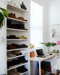 Home office with a desk, laptop, plant, and shelves of shoes and clothes on hangers.