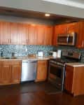 Wooden kitchen cabinets, stainless steel appliances, and mosaic tile backsplash in a modern kitchen.