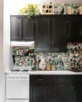 Black kitchen cabinets with floral wallpaper, white stove, and countertop with jars and utensils.