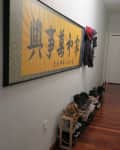 Narrow hallway with wooden floor, yellow framed artwork, coats hanging, and shoes lined up along the wall.