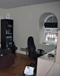 Living room with brown recliner, gray sofa, tall lamp, bookshelf, desk, and arched window.