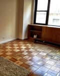Empty room with parquet flooring, a small table with a lamp, a cardboard box, and a window with a wooden shelf.