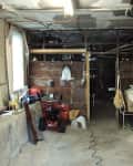 Cluttered basement with exposed pipes, storage boxes, a red snowblower, and an American flag on the wall.