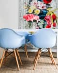 Dining area with blue chairs, white table, pink flowers, and floral wall art.