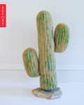 Artificial cactus sculpture with three arms, textured surface, and green accents on a stone base.
