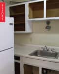 Outdated kitchen with white cabinets, open shelves, stainless steel sink, and white refrigerator.