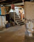 Basement with exposed brick, toilet, stairs, storage shelves, and various household items.