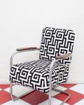 Retro chair with black and white geometric pattern, metal frame, and wooden armrests on red and white checkered floor.