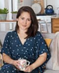 Woman in a blue dress sitting on a sofa with patterned pillows, holding a colorful mug.