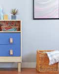 Wooden dresser with blue drawers, books, and a plant on top, next to a wicker basket with a striped blanket.