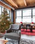 Loft living room with a Christmas tree, gray sofa, armchair, and dining table set on a red rug.