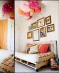 Cozy bedroom with pallet bed, colorful pillows, wall art, and hanging paper lanterns and pom-poms.