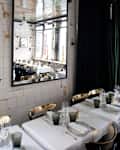 Elegant restaurant with white tablecloths, gold chairs, and a large wall mirror reflecting the dining area.