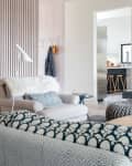 Cozy living room with a gray armchair, patterned cushions, and a white floor lamp, leading to a modern kitchen.