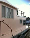 Pink houseboat with large windows, brown railing, and cushioned seating on the deck.