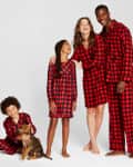 Family in matching red and black plaid pajamas, with a child petting a puppy.
