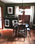 Dining room with dark wood table, four chairs, sideboard, chandelier, and framed art on olive green walls.
