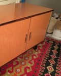 Wooden cabinet with two doors and metal handles on a colorful patterned rug, labeled "Before."