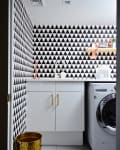 Laundry room with black and white triangle wallpaper, white cabinets, gold handles, and a washing machine.