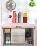 Open pink retro fridge with butter, eggs, milk, and half & half on shelves; cookbooks and decor on top.
