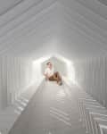 Person sitting in a geometric white tunnel with sunlight casting shadows.