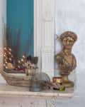 Marble mantel with a crystal ball, feather quills, driftwood, and a bronze bust, reflecting a blue wall with lights.