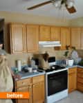 Cluttered kitchen with oak cabinets, ceiling fan, and a person holding a paper bag.