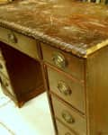 Vintage wooden desk with ornate drawer handles and a worn surface.