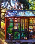 Stained glass greenhouse in a forest setting with colorful plant and mushroom designs on the panels.