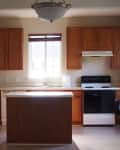 Kitchen with wooden cabinets, white appliances, and a central island under a ceiling light.