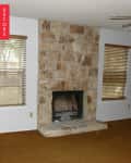 Stone fireplace in a living room with brown carpet and wooden blinds on windows.