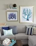 Gray sectional sofa with blue and white pillows, coral artwork, and a wooden coffee table with a decorative tray.