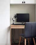 Compact home office with a wooden desk, black chair, monitor, desk lamp, and cactus decor.