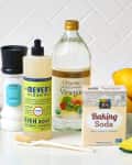 Cleaning supplies on a counter: sea salt, dish soap, vinegar, baking soda, lemons, sponge, and brush.