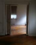 Open doorway leading to an empty room with wooden floors and a curtained window.