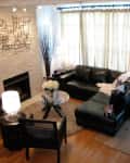 Living room with black leather sectional, glass coffee table, white flowers, wall art, and two cats on the sofa.