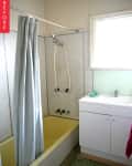 Small bathroom with yellow bathtub, gray shower curtain, white sink cabinet, and green washcloth.