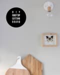 Round and house-shaped wooden cutting boards on a countertop, with a framed butterfly and light fixture above.