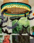 Hanging paper bats from a woven lampshade in a festive room with Halloween decor.