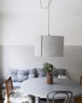 Gray dining area with round table, vase of flowers, cushioned bench, and pendant light.