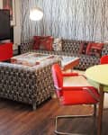 Retro living room with patterned sofa, red chairs, round table, and tree-themed wallpaper.