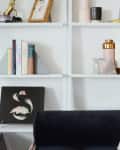 White shelves with books, art, and decor items above a dark sofa with patterned pillows.