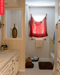 Bathroom with double sinks, red curtain over window, and beige cabinets.